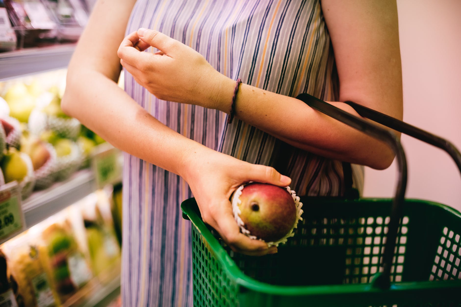 woman putting red apple on green shopping basket