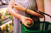 woman putting red apple on green shopping basket